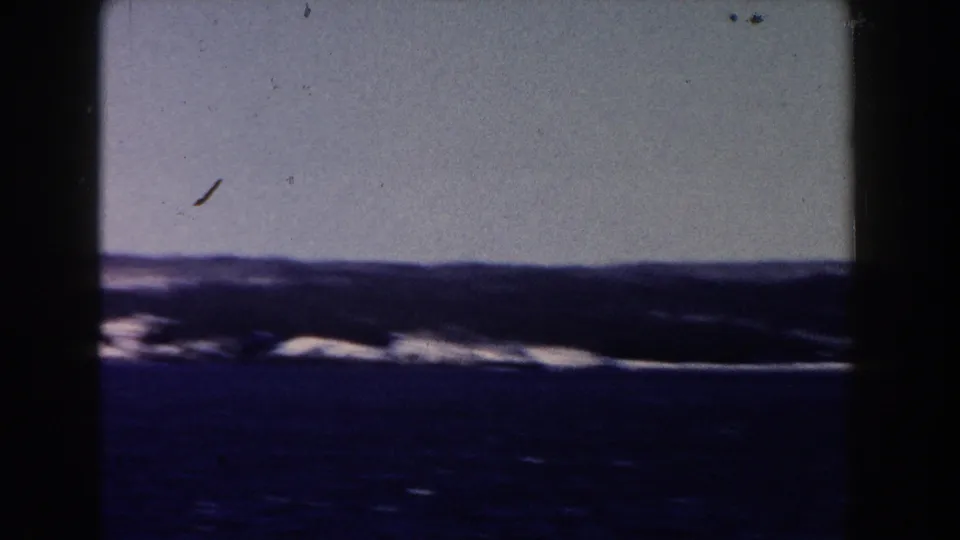 1960 8mm home-movie frame showing distant white-capped water beneath a pale sky, with visible film gate edges.