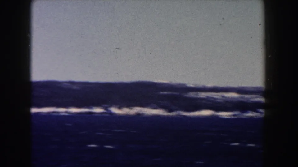 Handheld 1960 8mm frame of rough-looking water and a low horizon, with no people or structures visible.
