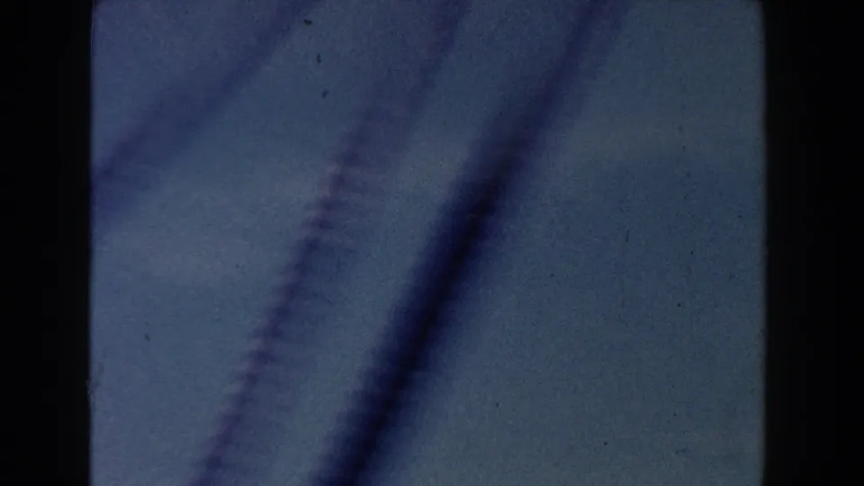 Motion-blurred 8mm frame with dark diagonal streaks, likely from helicopter rotor movement or rapid camera motion against the sky.