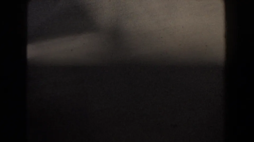 1960 Dearborn home-movie frame with dark exposure, soft blur, a pale horizontal area, and visible film grain.