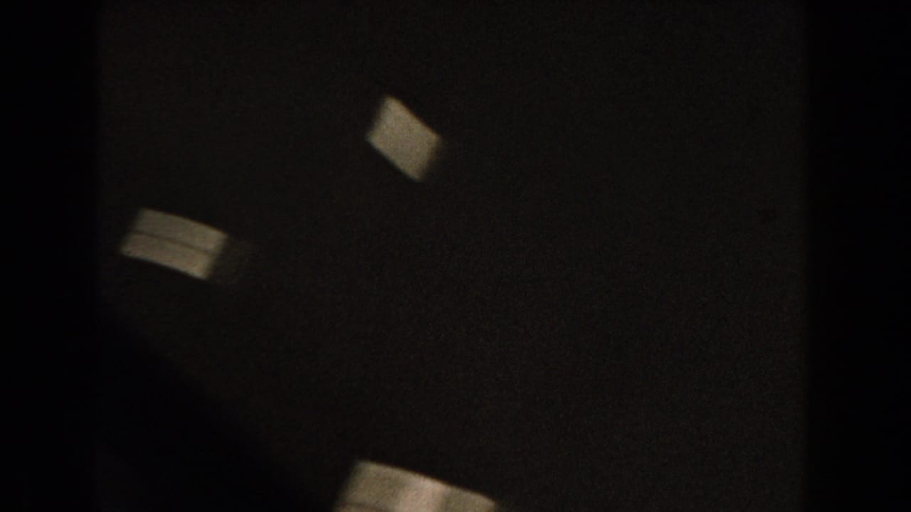 Dark, blurry frame with pale rectangular light shapes near the upper left.