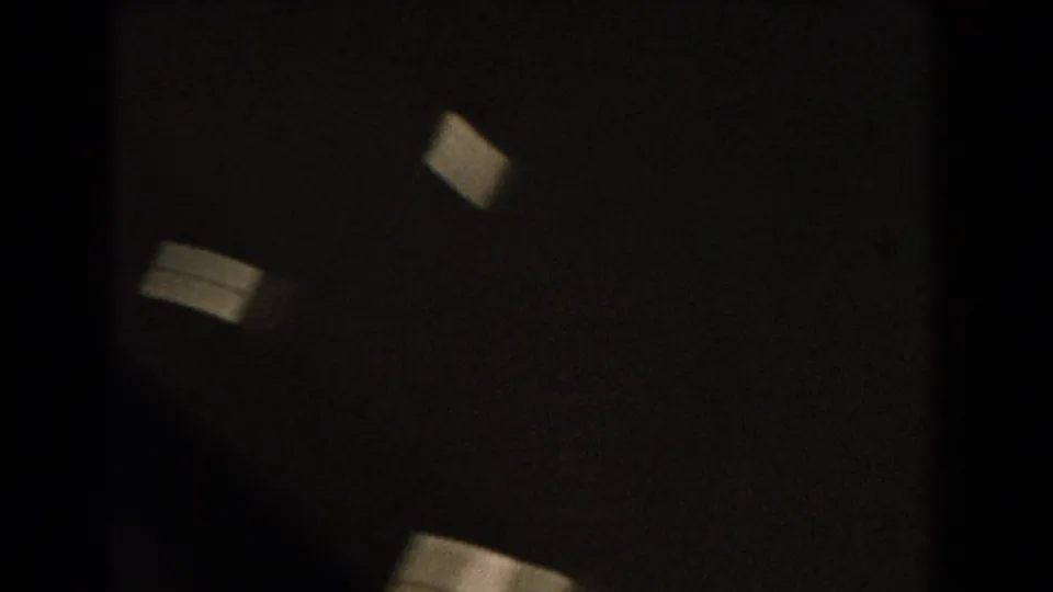 Abstract opening frame from the 8mm clip, with dark exposure and small pale shapes before the helicopter view becomes clear.