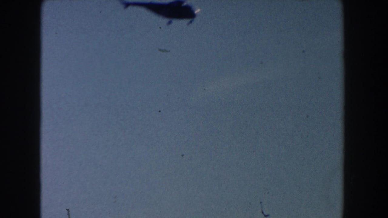 A distant helicopter silhouette appears high against a pale sky in the 1960 Dearborn, Michigan home-movie footage.