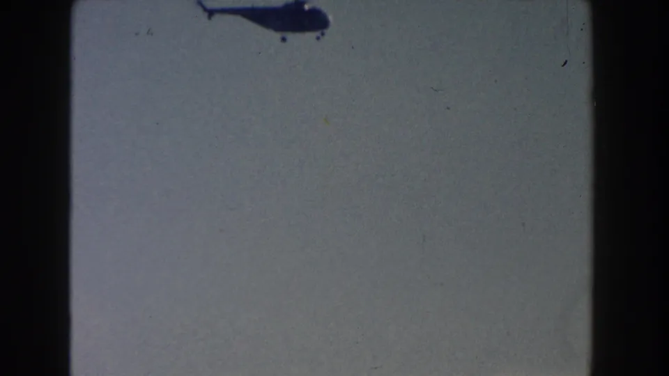 The helicopter is partly cropped near the top of the frame, leaving mostly open sky and visible 8mm film texture.