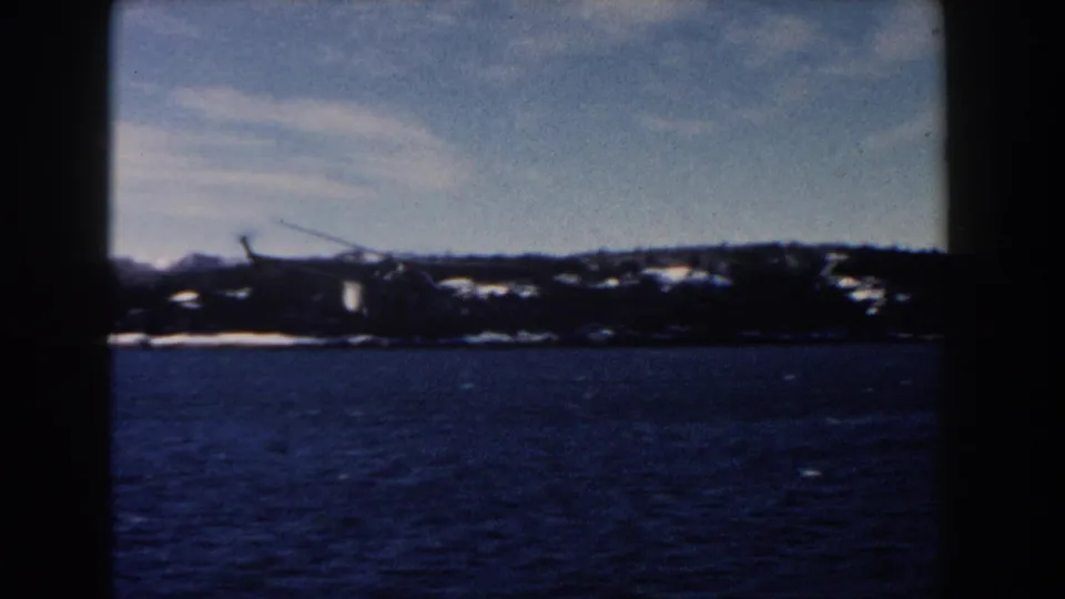 Helicopter above a distant winter shoreline, partially divided by a dark window or film-frame edge in this 1960 home-movie view.