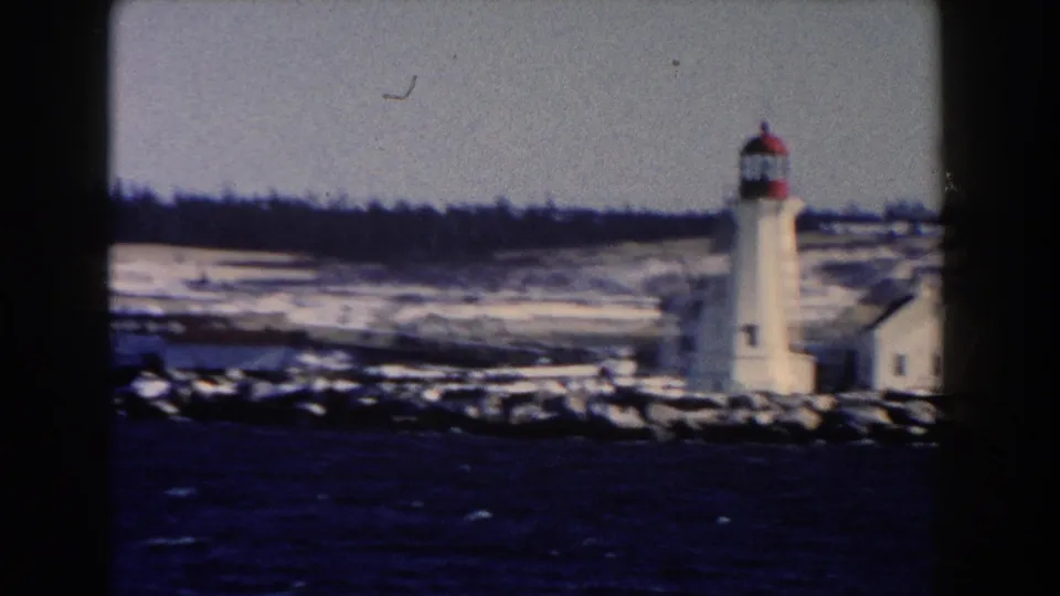 1960 8mm view of a white lighthouse with red lantern room on a snowy waterfront near Dearborn, Michigan.