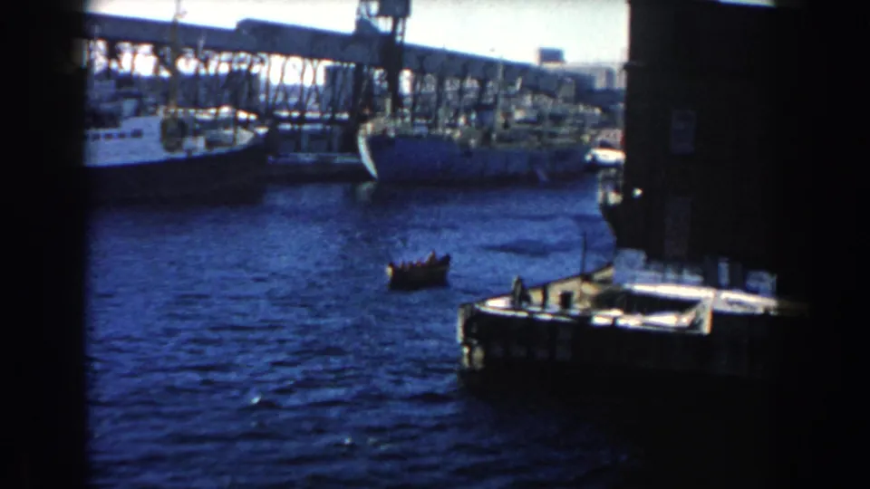 Small rowboat on blue harbor water near larger vessels and industrial waterfront structures in Dearborn, Michigan.
