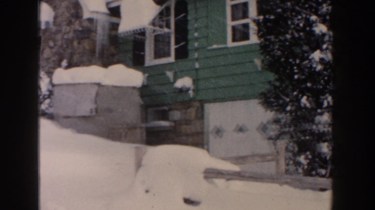 Closer view of snowbanks beside a green house and light garage door.