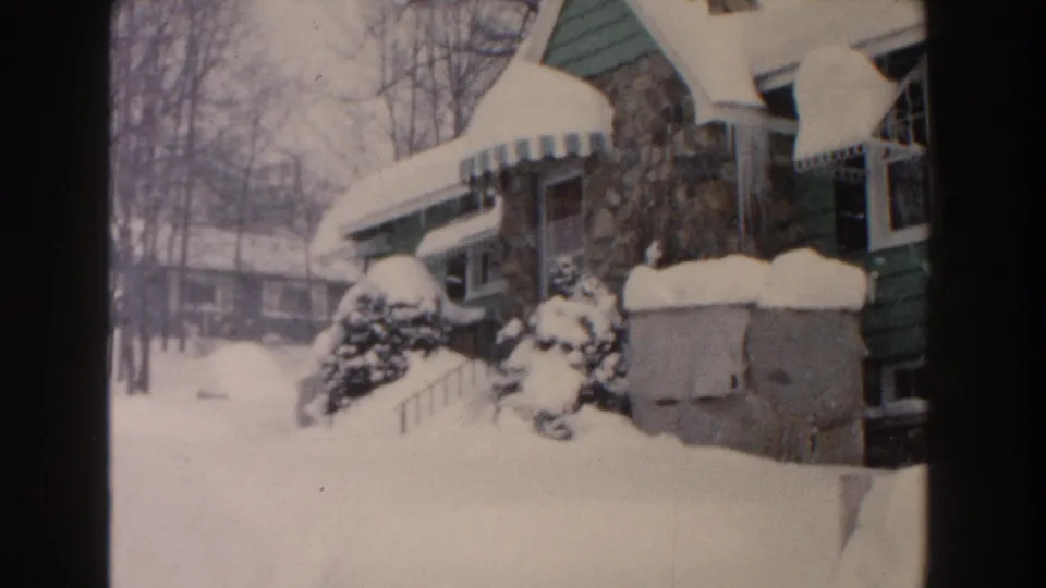 Wide 8mm frame from Dearborn, Michigan, showing a residential street-side yard buried in snow beside a green-sided house.