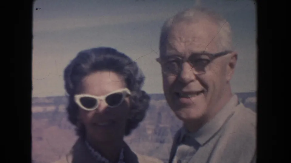 An older couple smiles in a close 8mm frame at an Arizona canyon overlook, with soft color and visible film wear.