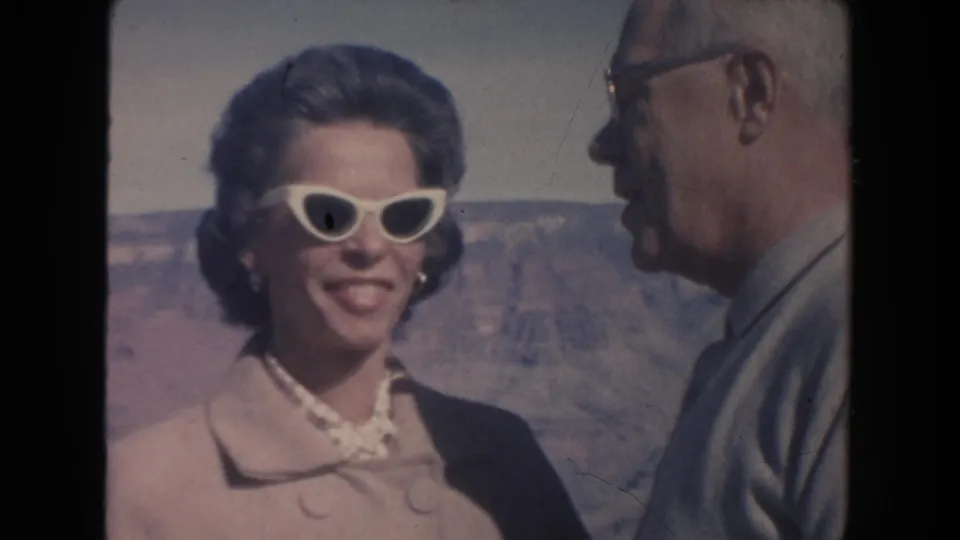 1962 Arizona frame of a smiling woman in white sunglasses beside an older man at the Grand Canyon overlook.
