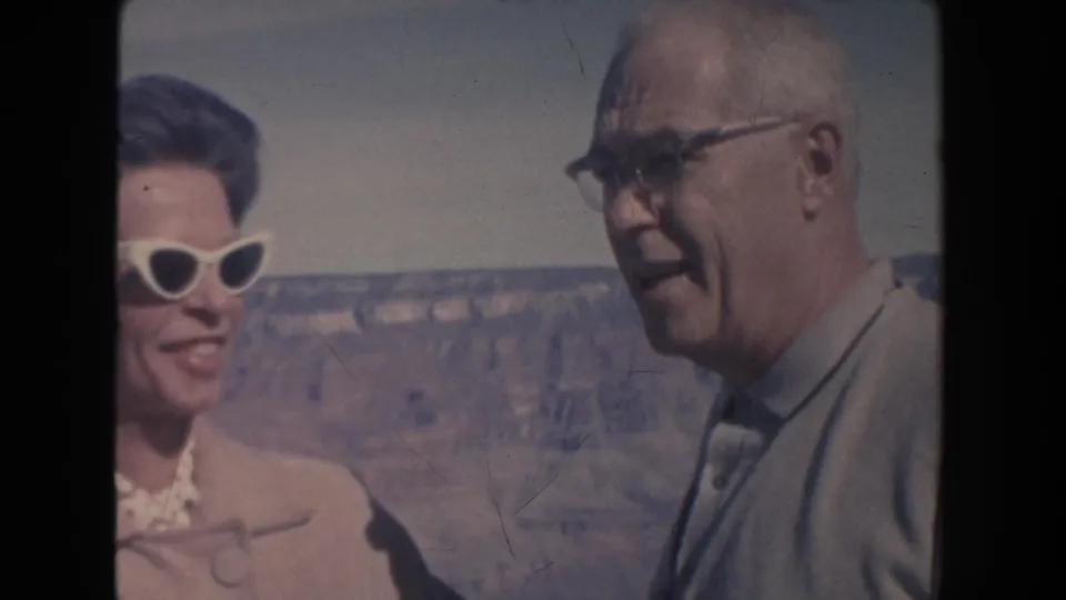 1962 Arizona home-movie still with an older man in glasses speaking beside a partly cropped woman at the Grand Canyon.