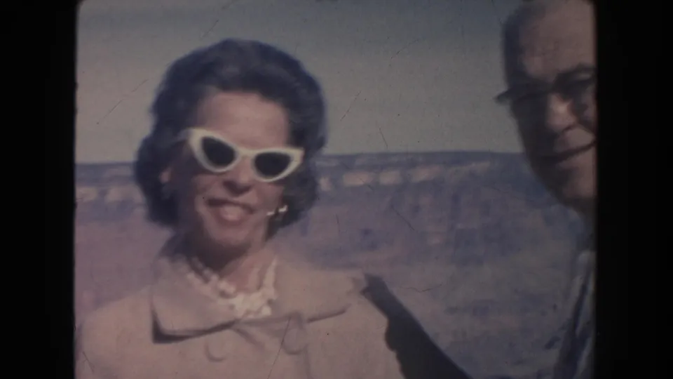 1962 Arizona frame showing the woman smiling in white sunglasses as her companion is partly cropped near the Grand Canyon.