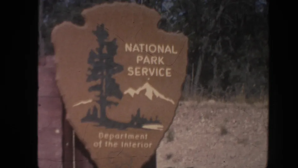1962 Arizona home-movie frame showing a National Park Service arrowhead sign near the Grand Canyon entrance.