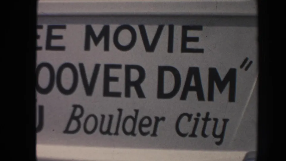 Close 1962 Arizona frame of a Boulder City sign advertising a Hoover Dam movie, with bold block type and cursive place text.