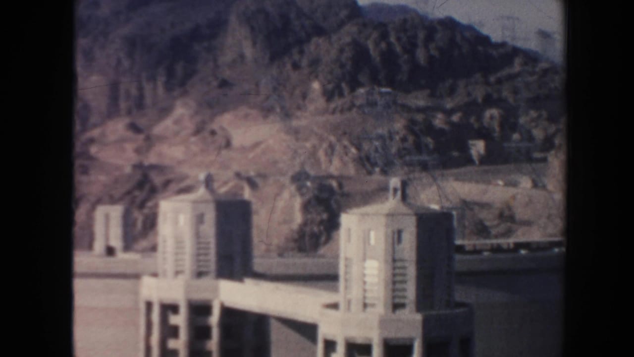 Concrete intake towers stand near rocky mountains at a dam site.