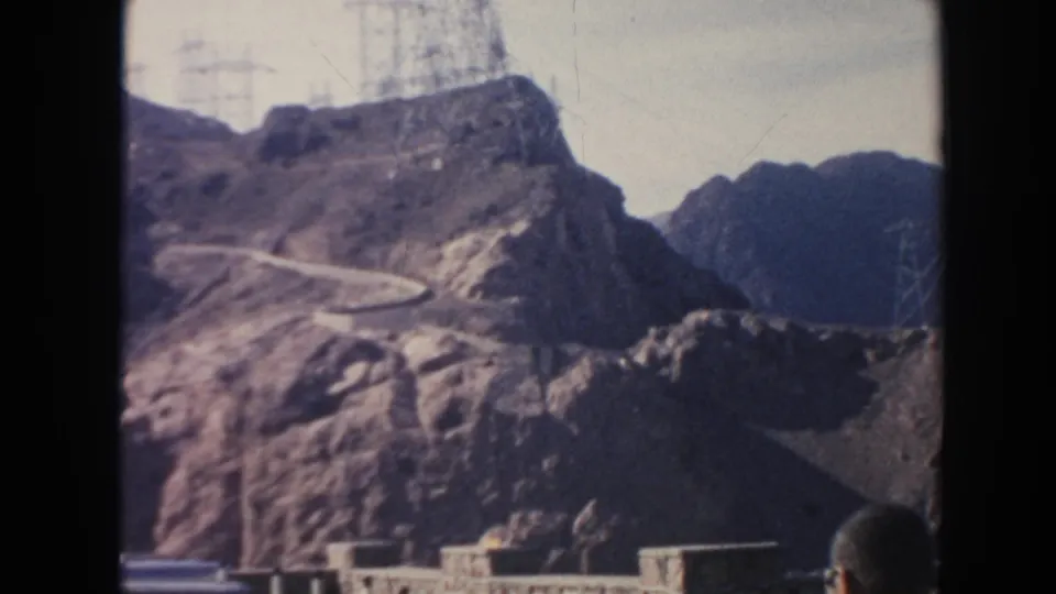A faded 8mm view of an Arizona dam landscape, with transmission towers on a rocky ridge and concrete structures below.