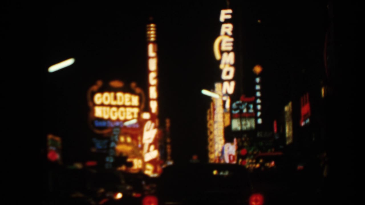 Soft nighttime view of Golden Nugget and Fremont neon signs along a dark street.