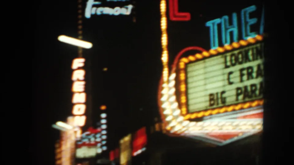1962 8mm frame showing a glowing theater marquee near the vertical Fremont sign in a nighttime commercial street.