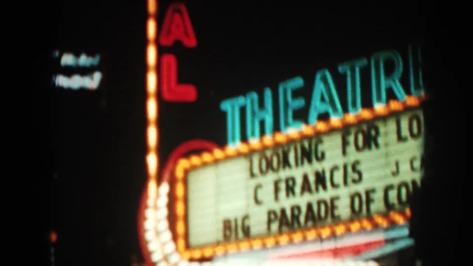 1962 8mm frame with a close view of an illuminated theater marquee and partial readable lettering under neon signs.