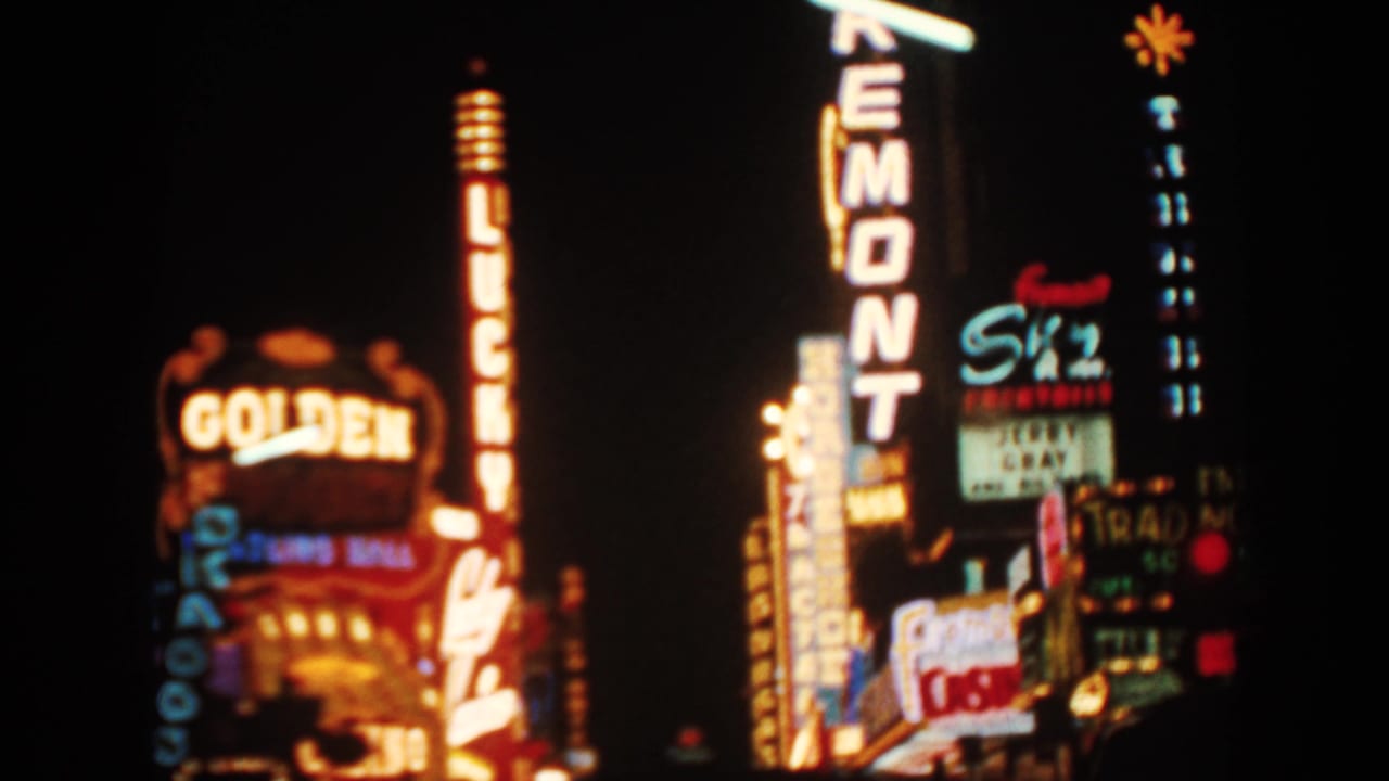 1962 8mm view of bright casino-district neon signs against a dark night sky, including Golden Nugget and Remont signage.