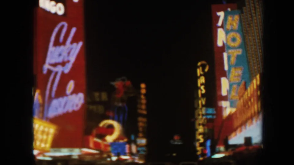 1962 8mm night frame with a vertical HOTEL sign, Lucky Casino signage, and Golden marquee lights in a tourist district.