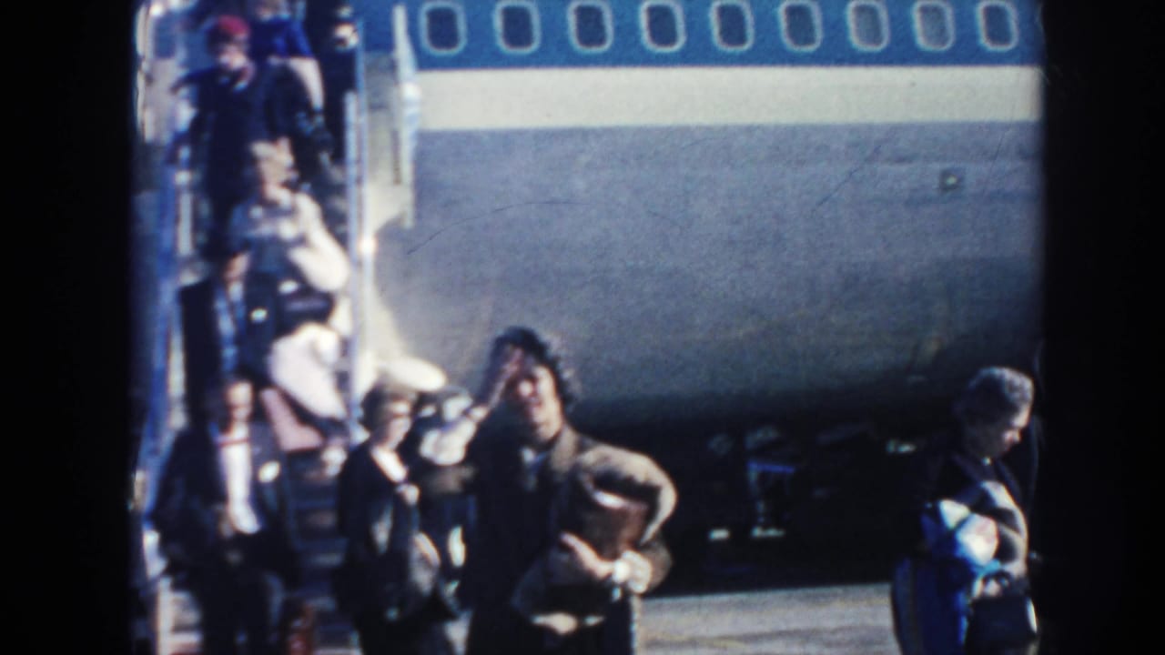 Passengers cluster near the stairway of a blue-and-white Pan American aircraft on a bright airport ramp in Arizona.