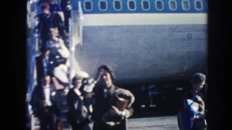 Passengers cluster near the stairway of a blue-and-white Pan American aircraft on a bright airport ramp in Arizona.