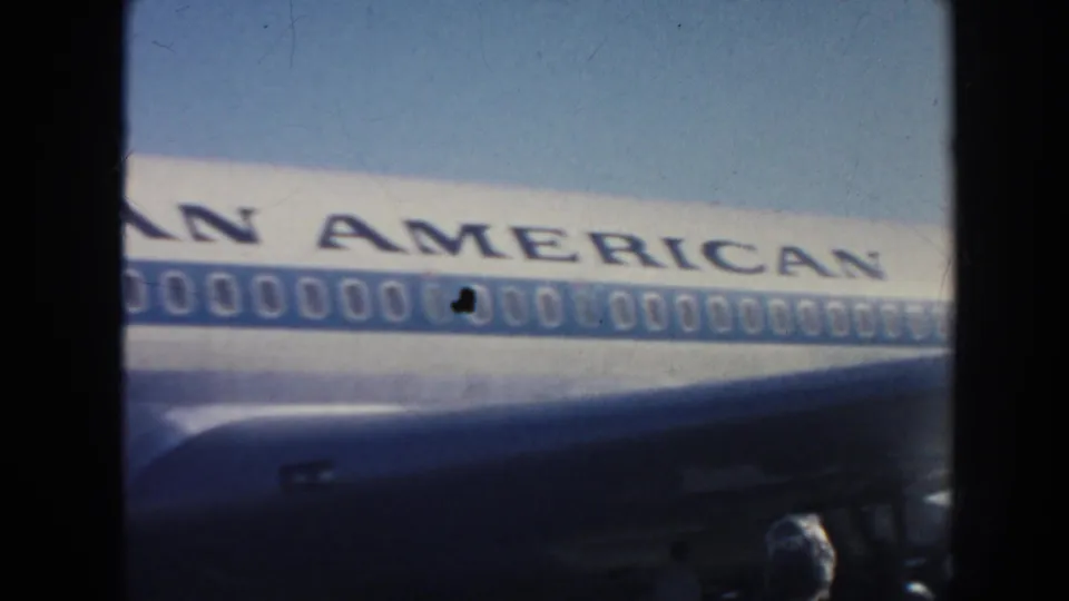1962 home-movie frame showing a Pan American jet parked on a sunlit runway, with fuselage lettering and windows visible.