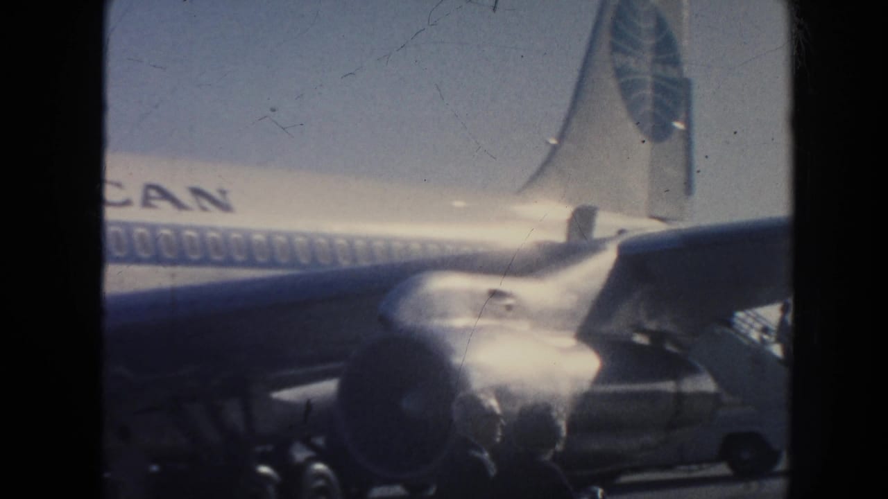 A Pan American jet remains parked in view, with the wing and engine area partially visible through sun glare and 8mm film softness.
