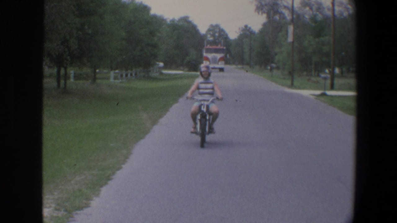 Young woman rides a small motorbike toward the camera on a tree-lined suburban road.