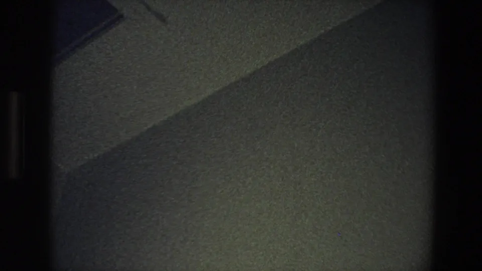 1973 Minnesota 8mm frame showing a dim textured interior wall crossed by a diagonal shadow line.