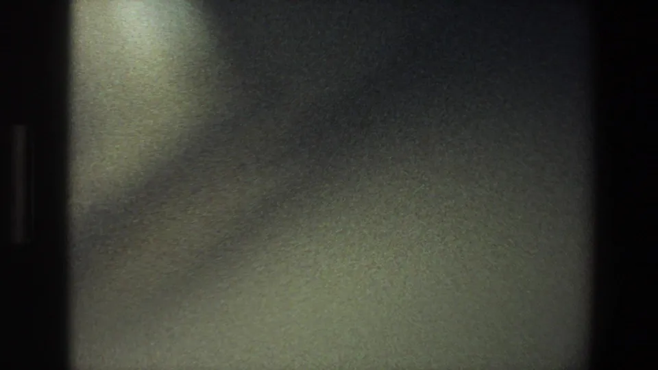 1973 Minnesota 8mm frame with soft focus on a dark interior wall and a pale light patch above.