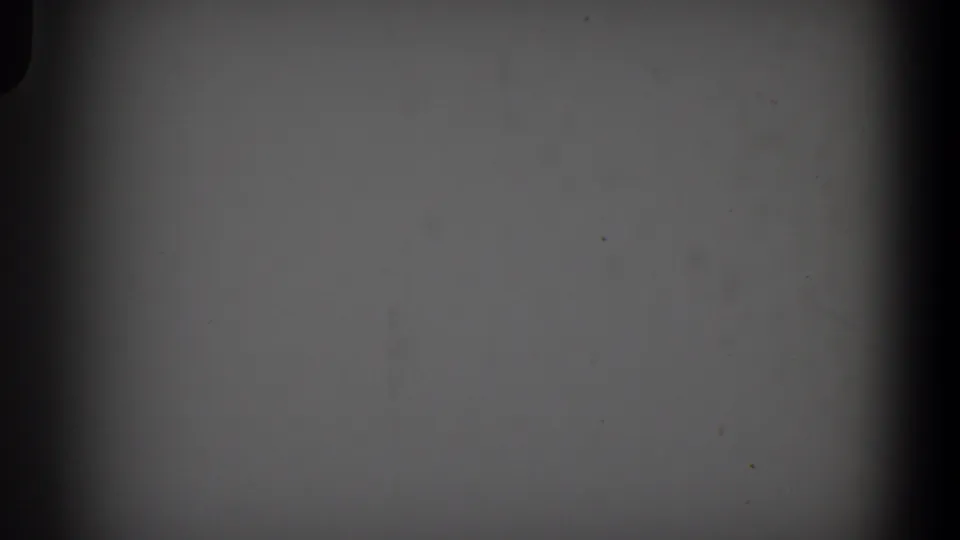 1958 Lubbock 8mm frame showing a blank pale gray field with dark film edges, dust specks, and uneven exposure.