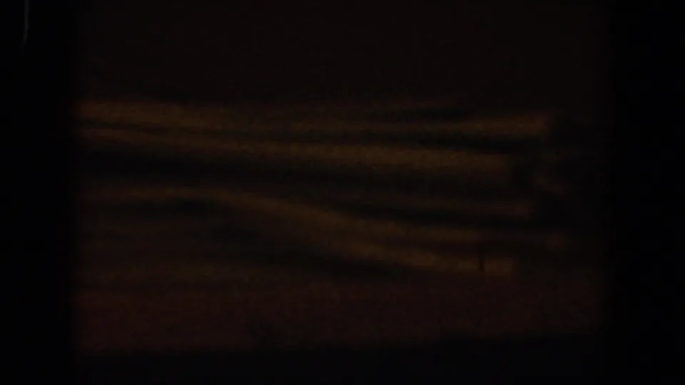 Dark 1958 Lubbock, Texas 8mm frame with faint orange light, indistinct horizontal forms, and heavy shadow across the view.