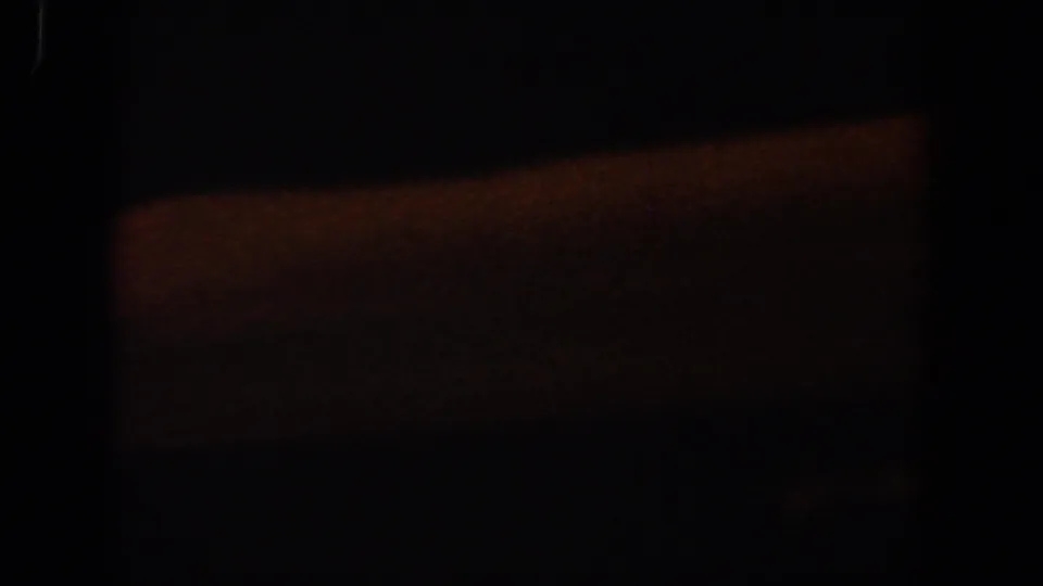 Very low-light 8mm frame from the Lubbock clip showing a soft orange rectangular area surrounded by heavy darkness.