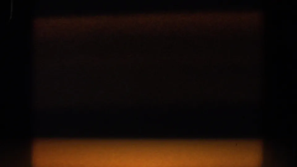 Out-of-focus 1958 8mm frame with dark vertical shapes and a warm orange light band near the bottom of the frame.