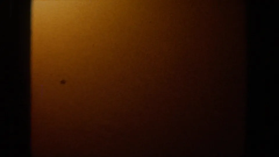 Low-exposure 8mm frame from the Lubbock footage showing a broad orange surface, small dark mark, and deep shadow around the edges.