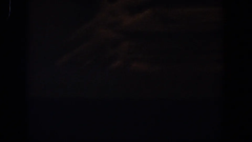 1958 Lubbock 8mm frame showing a dark lower room area with indistinct folded or stacked objects below a pale ledge.