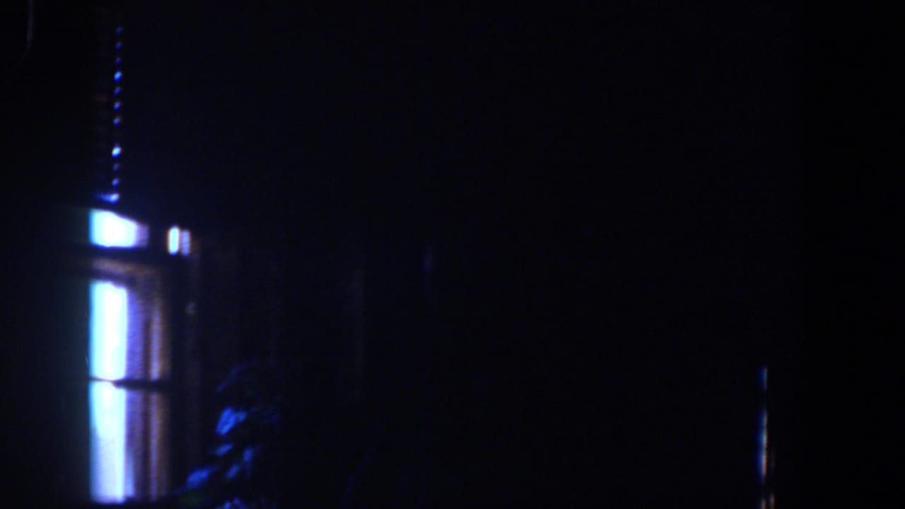 1958 Lubbock home-movie frame showing a very dark interior lit by narrow blue-white window panels and faint room shapes.