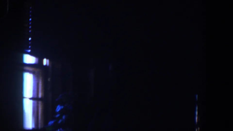 1958 Lubbock home-movie frame showing a very dark interior lit by narrow blue-white window panels and faint room shapes.