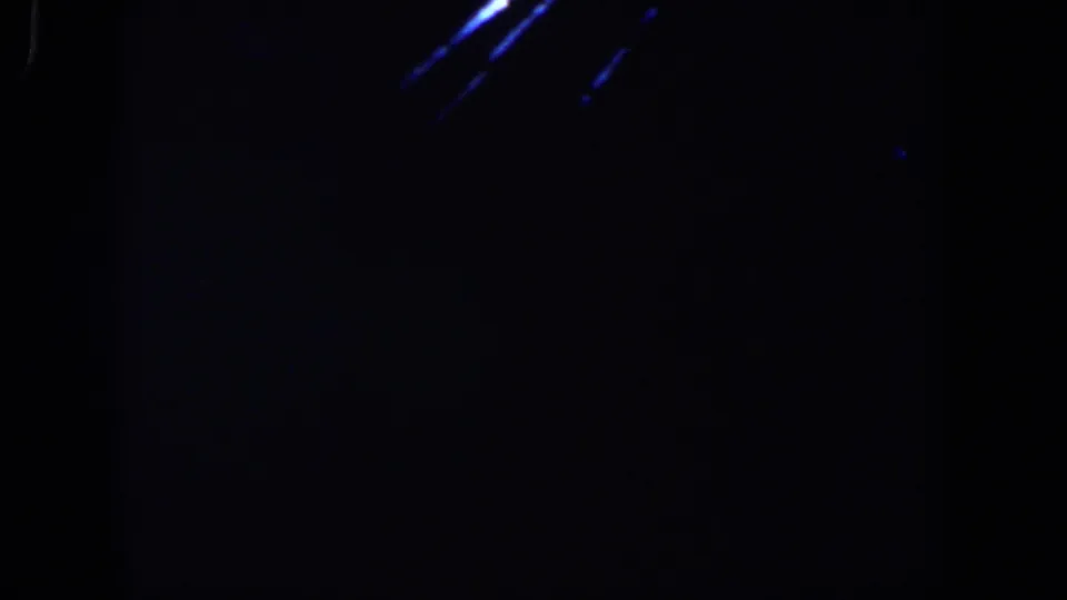 Shaky 8mm frame from Lubbock with blue light streaks cutting through a mostly black interior view.
