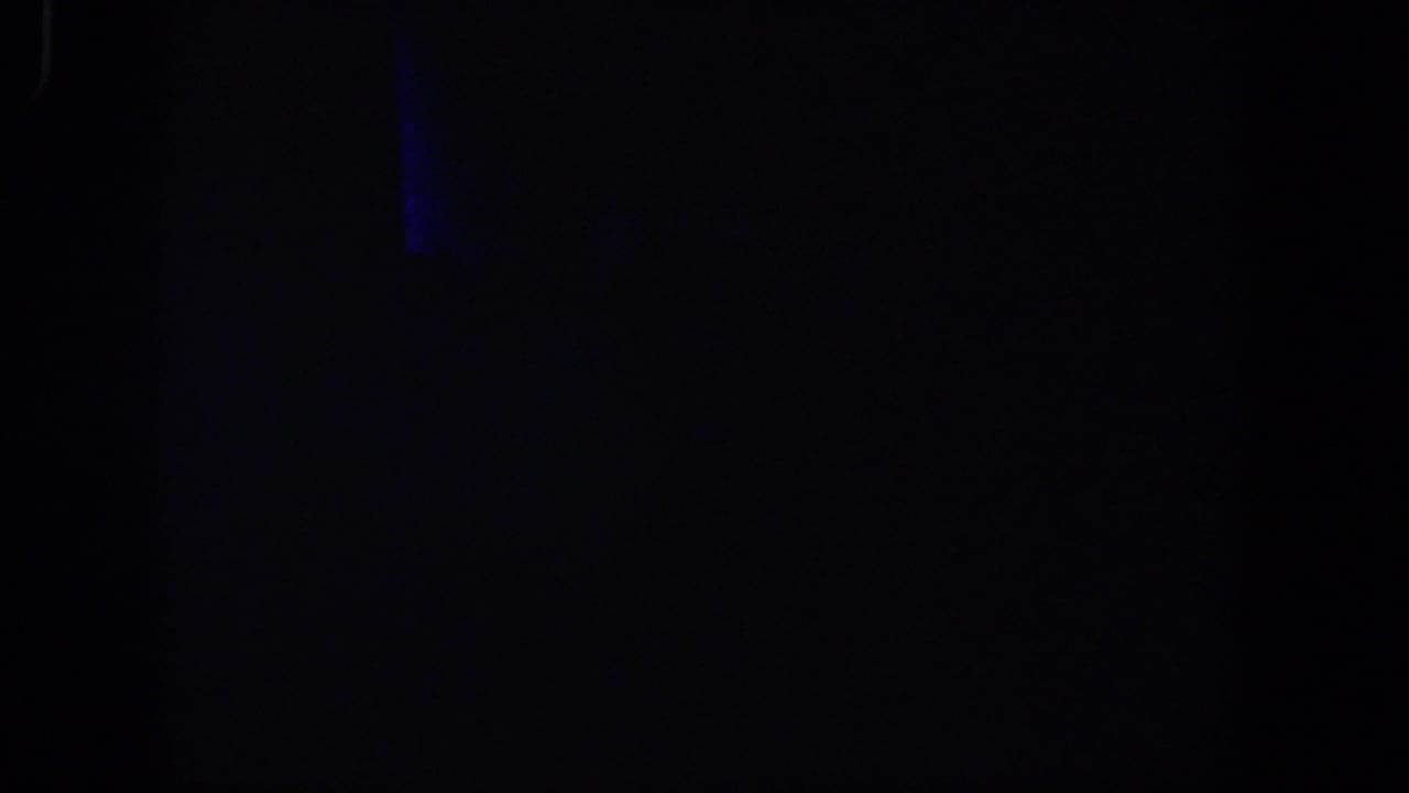 Very dark 1958 8mm frame from Lubbock, Texas, with a faint blue light or reflection near the upper left and minimal visible detail.