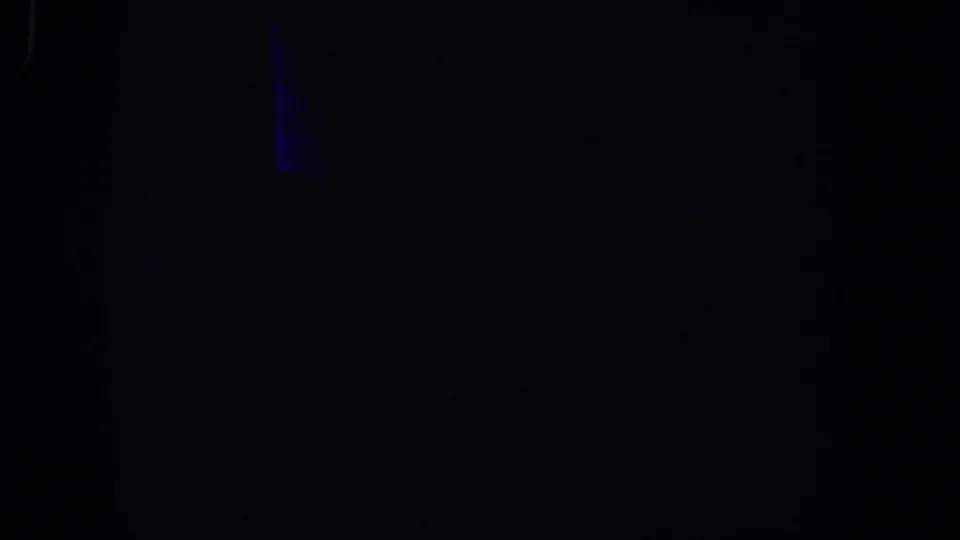 Very dark 1958 8mm frame from Lubbock, Texas, with a faint blue light or reflection near the upper left and minimal visible detail.