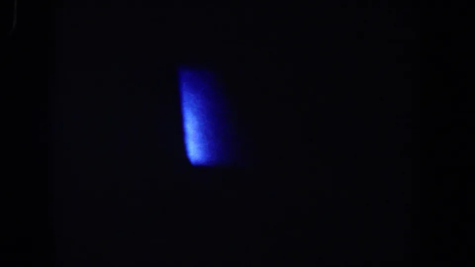 Underexposed 8mm frame with a bright blue patch near the upper right, with surrounding interior detail largely obscured by darkness.