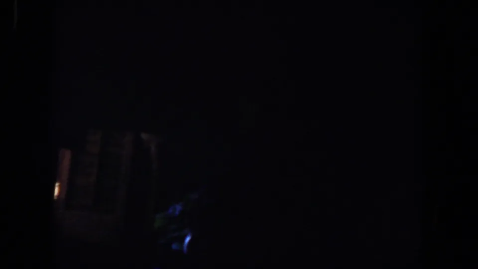 Very dark 8mm frame with faint blue highlights near the lower right and indistinct interior forms, likely part of the same dim scene.