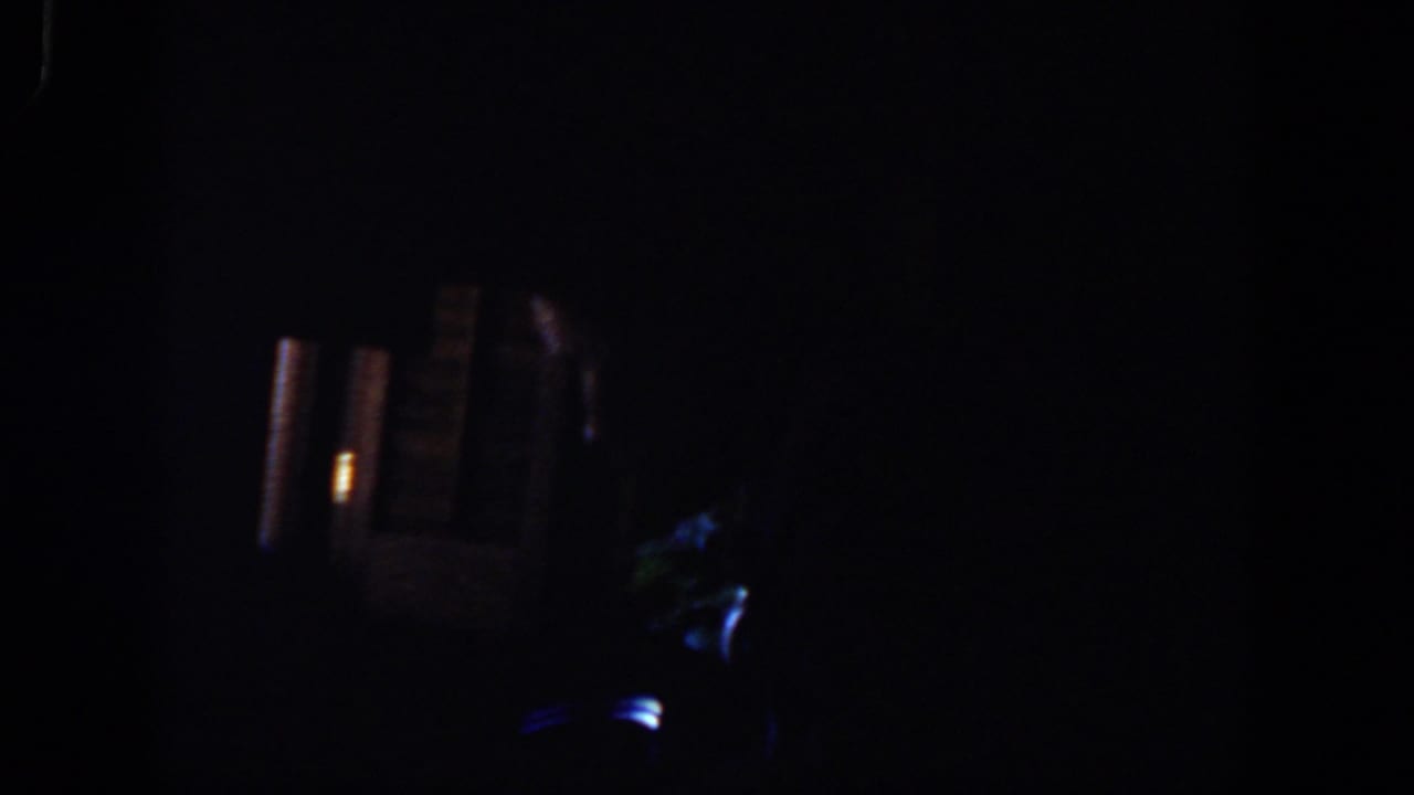 Very dark frame with faint blue reflections and warm vertical light patches.