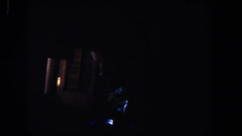 Underexposed 1958 Lubbock home-movie frame showing deep shadows, small blue glows, and warm light shapes in an unclear interior.