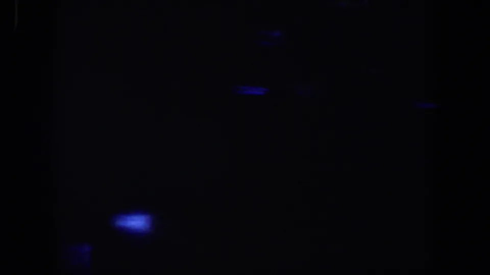 Underexposed home-movie frame from the Lubbock reel with a stronger blue glow near the lower left and little readable detail.