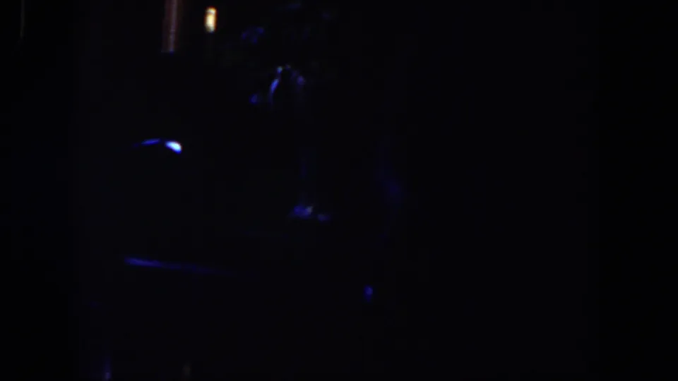 Dim 1958 Lubbock home-movie frame with scattered blue highlights and indistinct forms, possibly inside a dark room.